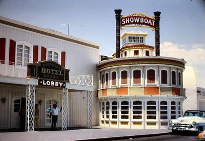 The Showboat's riverboat facade in 1968: a red SHOWBOAT sign with gold bulb letters mounted between two black fluted smokestacks above the white round pilothouse structure, with the hotel lobby entrance at left and a powder-blue Cadillac parked at right